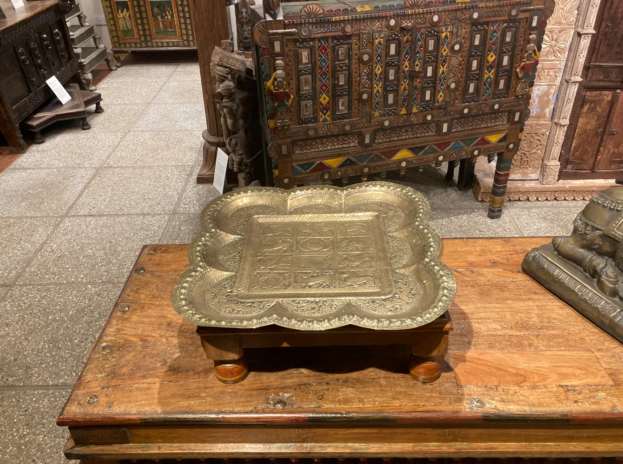 A picture of the tray on a wooden table taken in the gallery space. It is taken with the camera pointing down at a 45 degree angle. There are various decorative furniture pieces and objects on display in the background.