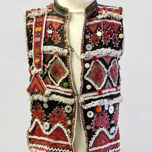 An intricate embellished child's waistcoat on a bust. It is red white and black in colour with lots of patterns, buttons, beadwork and stitching pattern throughout.