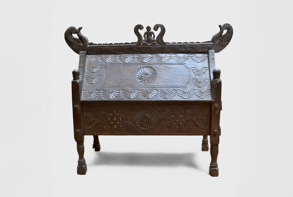 This shows a dark wood chest with short thin legs and ornate features and carving throughout.
