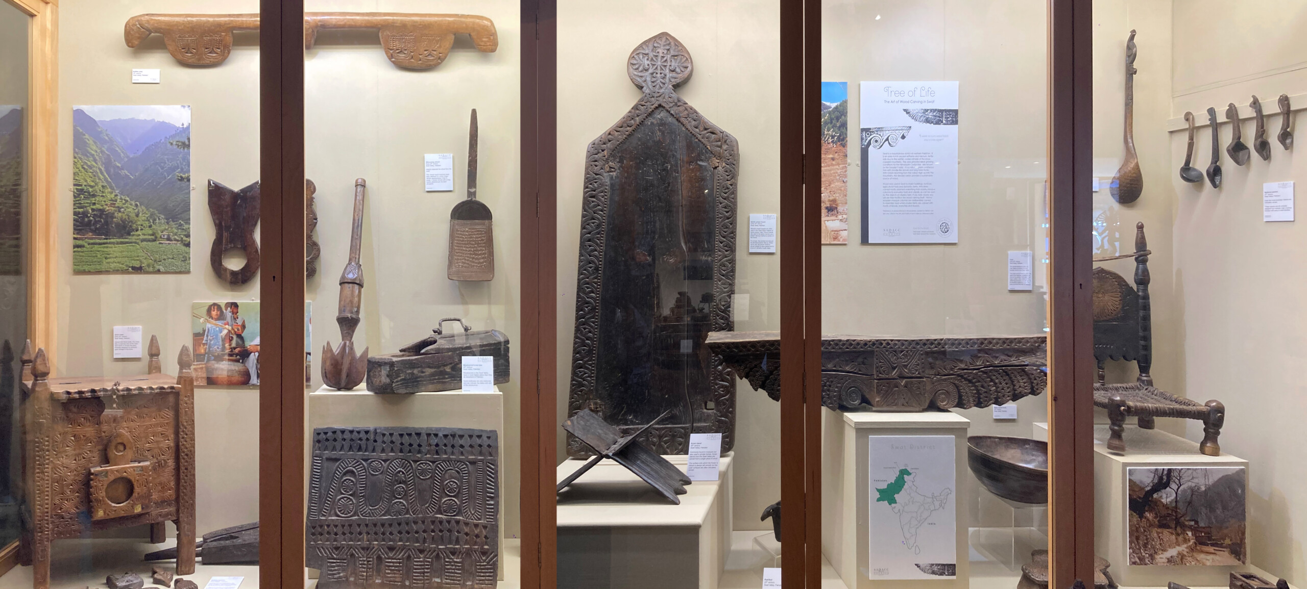 This image shows the case in full, it is well lit and has a lot of different types of hand carved wooden objects amongst interpretation on the walls.