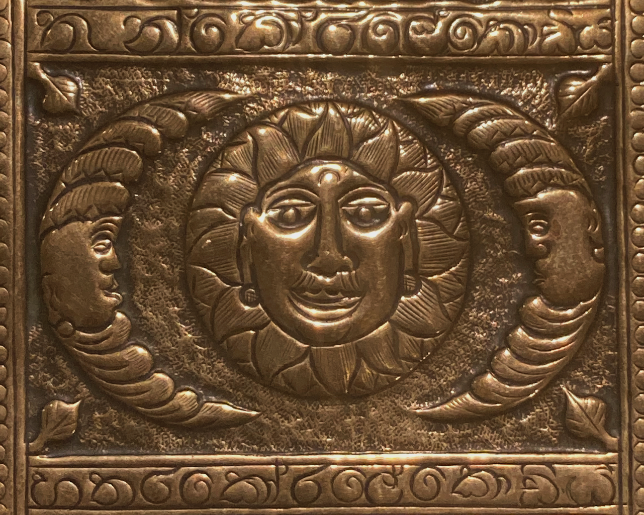 This shows a section of the tray. It is a central stylised sun and two crescent moons at each side. All have a face. There is an ornate border around this.