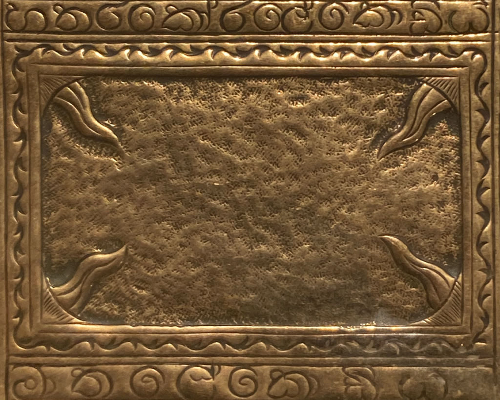 A section of the tray. It is a plain central panel with some light texture, there are lines coming down from the four corners. It has an ornate border around this symbol.