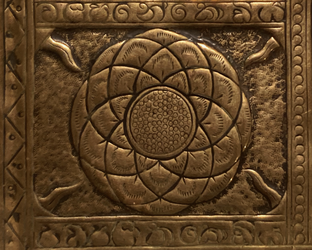 A close up of part of the tray. It is a geometric lotus flower. It is made up of many circles overlapping around a central dotted circle. There are lines coming in from the corners. There is an ornate border around this symbol.